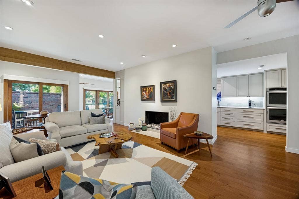 Open-concept living area featuring wood-finish flooring, a recessed fireplace with a stone hearth, exposed timber ceiling beam, sliding glass doors, and recessed lighting
