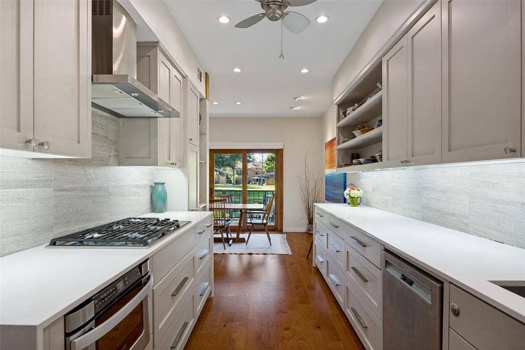 Galley kitchen featuring flat-panel cabinetry, white solid-surface countertops, horizontal-tile backsplash, stainless steel gas cooktop with range hood, and wood-finish flooring