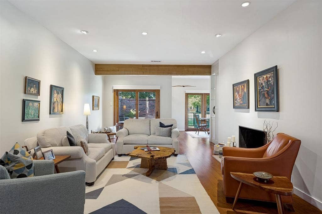 Living area featuring wood-finish flooring, exposed structural ceiling beam, recessed lighting, and a fireplace with a minimalist surround