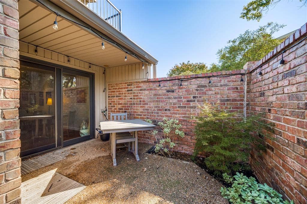 Private courtyard featuring red brick perimeter walls, a covered patio area, sliding glass doors, and established greenery