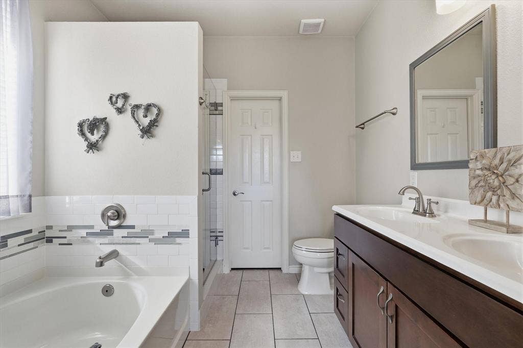 The updated primary bath brings together a soaking tub, double-sink vanity & separate glass-enclosed shower.