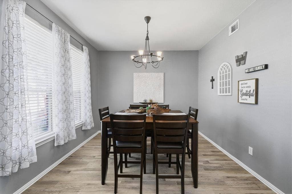 Tall windows bring natural light into the dining room, complemented by a chandelier & luxury vinyl plank flooring.
