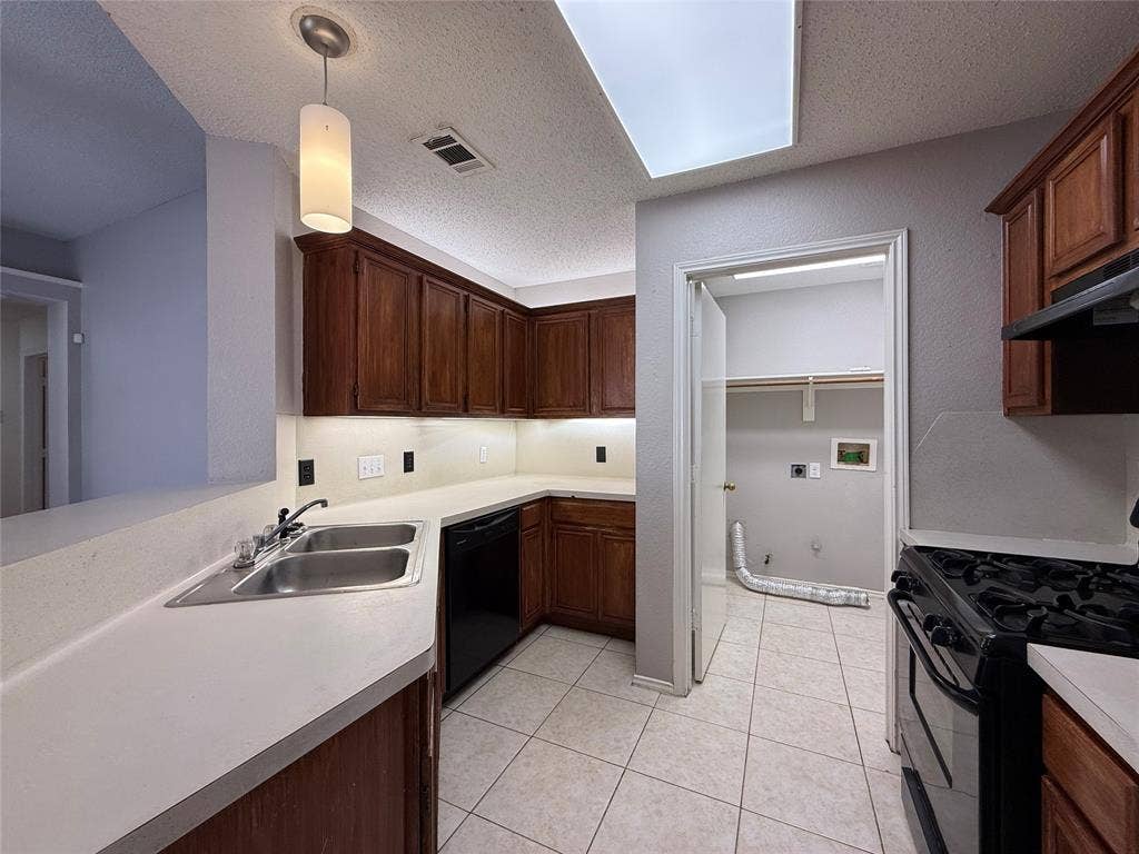 5210 Welbeck Court, Garland, TX 75043 Kitchen featuring stained wood cabinetry, solid surface countertops, dual-basin stainless steel sink, integrated recessed lighting, and tile flooring