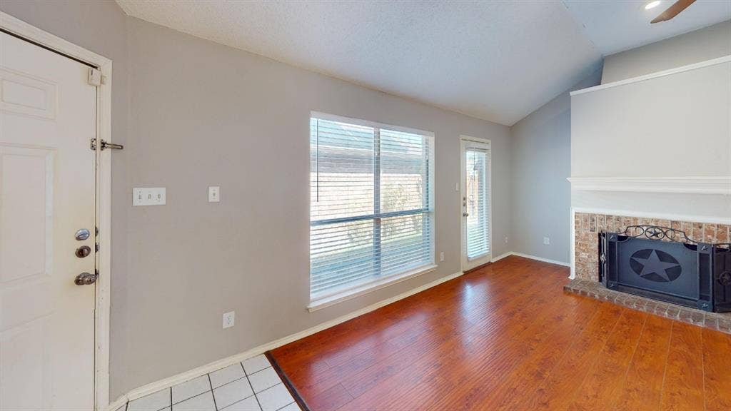 5210 Welbeck Court, Garland, TX 75043 Vaulted ceiling featuring a brick-surround fireplace with a wooden mantel, wood-finish flooring, and large windowed exterior door