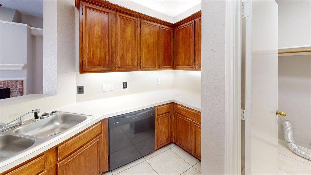 5210 Welbeck Court, Garland, TX 75043 Kitchen featuring stained wood cabinetry, solid-surface countertops, dual-basin stainless steel sink, black dishwasher, and tile flooring