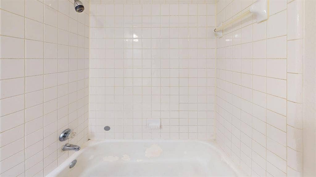 5210 Welbeck Court, Garland, TX 75043 Bathtub enclosure featuring white square tile surround, wall-mounted shower head, metal faucet hardware, and integrated soap dish