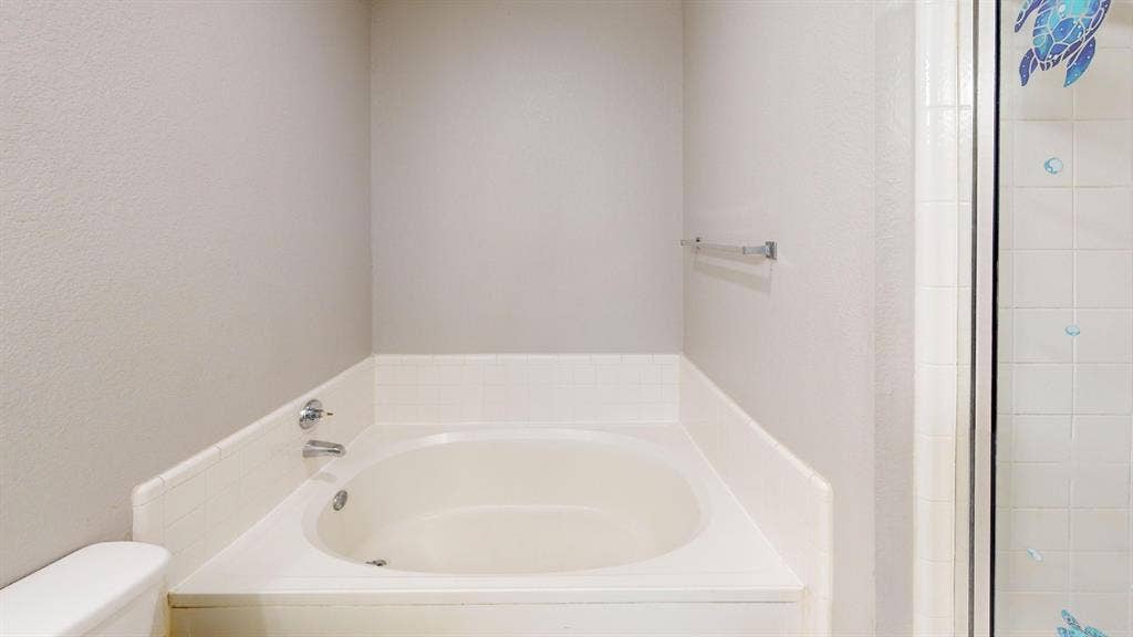 5210 Welbeck Court, Garland, TX 75043 Built-in soaking tub with white tile surround, chrome faucet hardware, and a glass-enclosed shower stall