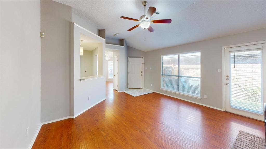 5210 Welbeck Court, Garland, TX 75043 Vaulted ceiling with a central brushed-nickel ceiling fan, wood-finish flooring, recessed wall niche, and glass-paneled exterior door