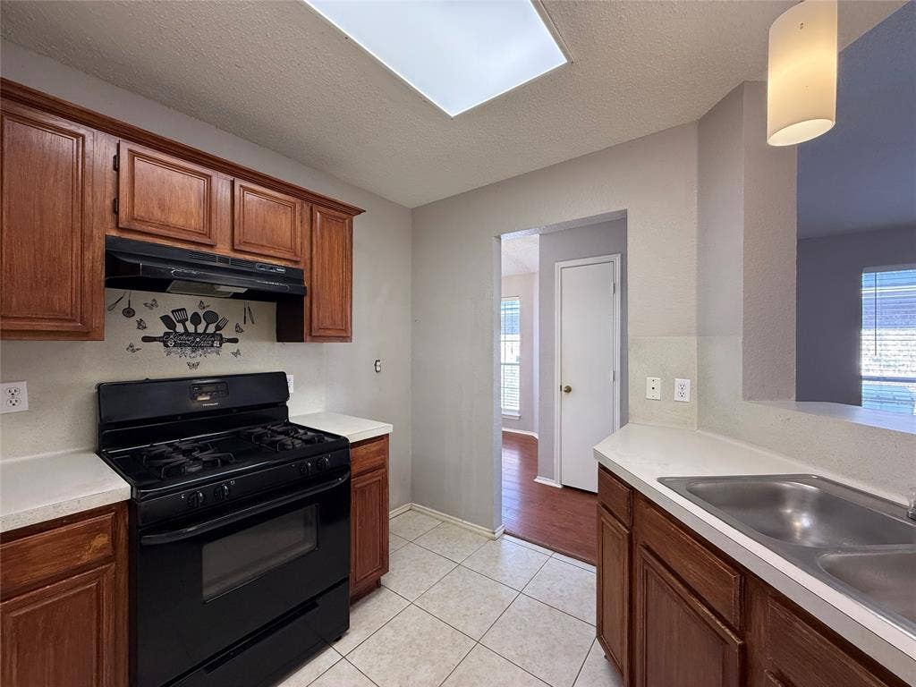 5210 Welbeck Court, Garland, TX 75043 Kitchen featuring wood cabinetry, solid-surface countertops, dual-basin stainless steel sink, black range, and ceramic tile flooring