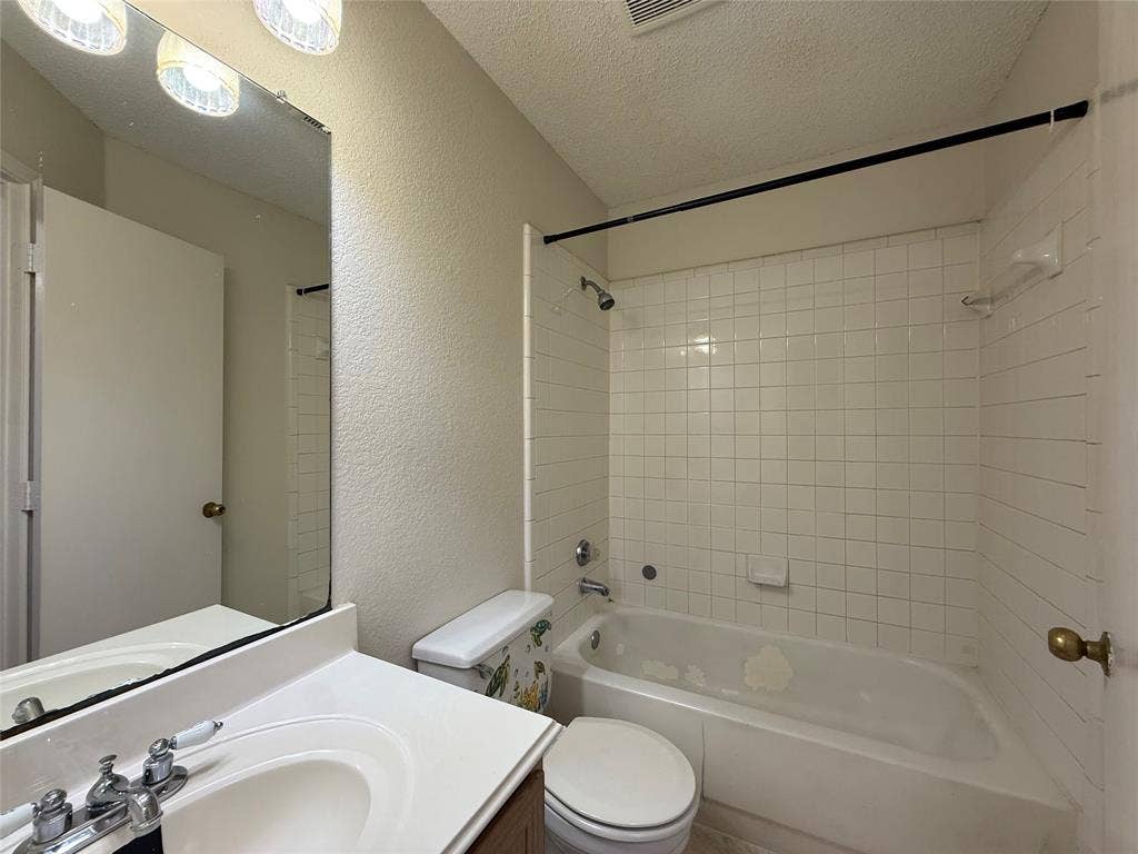 5210 Welbeck Court, Garland, TX 75043 Bathroom featuring a vanity with a white countertop and oval sink, a wall-mounted mirror, three-light overhead fixture, and a tub-shower combination with white wall tile