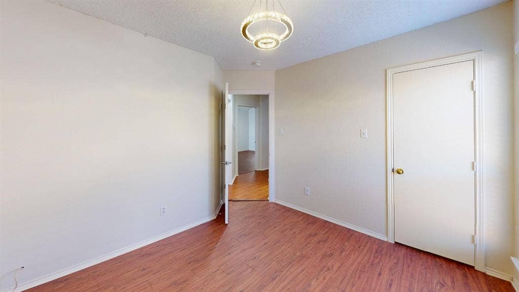 5210 Welbeck Court, Garland, TX 75043 Neutral-toned interior space featuring wood-finish flooring, a modern tiered chandelier, and a solid-core interior door