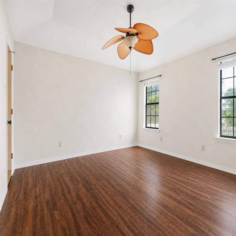 Vaulted ceiling room featuring wood-finish flooring, a multi-blade ceiling fan with integrated light, and grid-pattern windows with dark frames