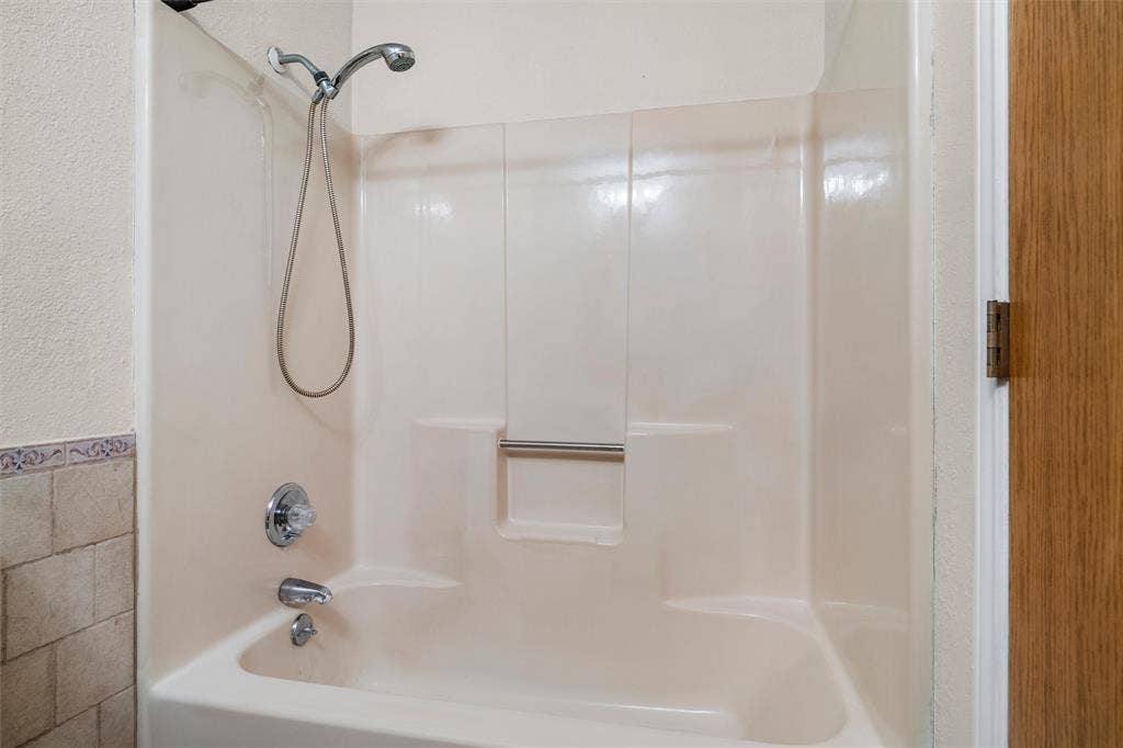 Tub-shower combination featuring a molded surround, integrated soap niche, handheld showerhead, and chrome-finished plumbing fixtures