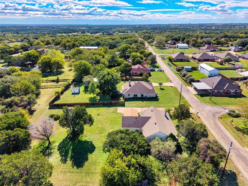 Aerial perspective of a sprawling property featuring expansive acreage, mature tree canopy, multi-level wood fencing, and a multi-pitched composition shingle roof