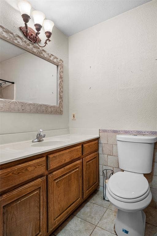 Bathroom featuring wood-finish cabinetry, an integrated sink with a chrome faucet, a decorative wall-mounted mirror, three-light overhead fixture, and tile wall accents