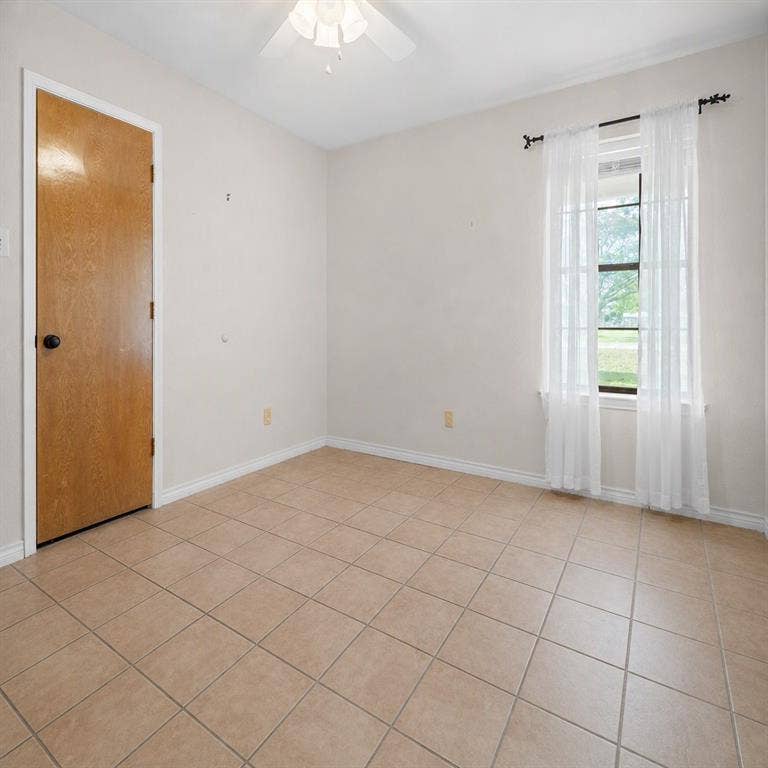 Ceramic tile flooring, neutral wall tones, single-panel wood door, and a ceiling fan with integrated lighting