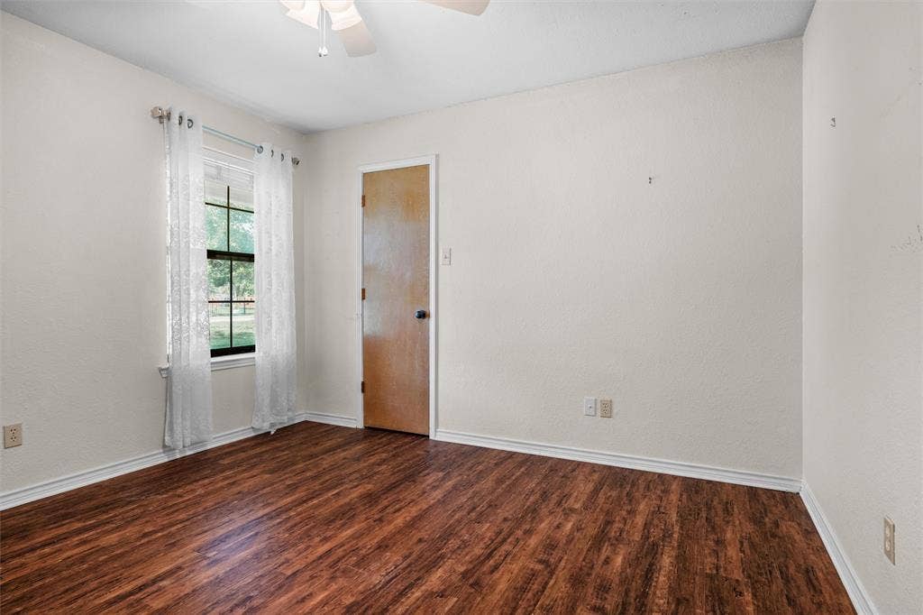 Room featuring wood-finish flooring, a single-hung window with a muntin grid, and a ceiling-mounted fan
