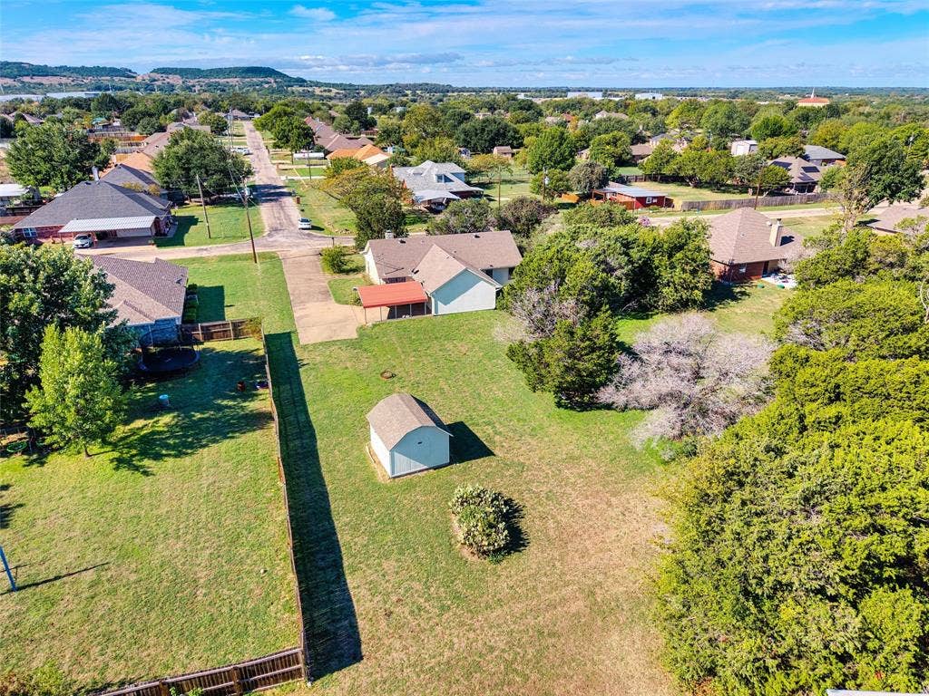 Expansive parcel featuring mature trees, a detached storage structure, wooden perimeter fencing, and concrete driveway access