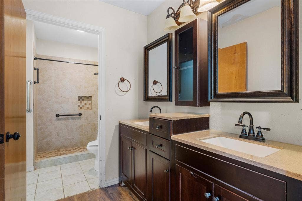 Double vanity featuring dark wood cabinetry, rectangular undermount sinks, neutral stone-finish countertops, and matching framed mirrors