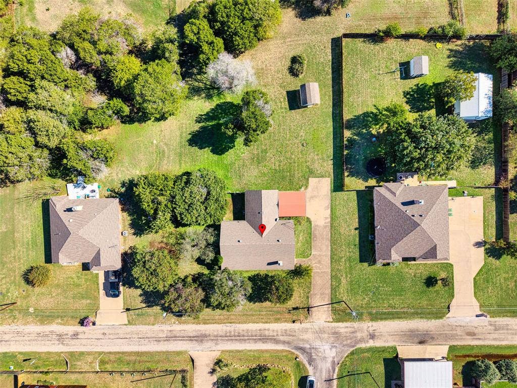 Aerial perspective of a residential property featuring an expansive lot, mature trees, a concrete driveway, and multiple detached storage structures