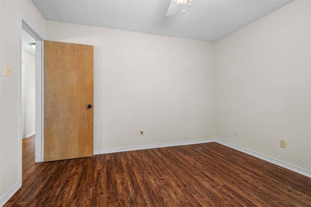 Interior room featuring wood-finish flooring, neutral wall paint, a solid wood-finish door, and a ceiling-mounted fan fixture