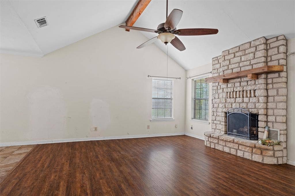 Vaulted ceiling with exposed wood beam, wood-finish flooring, and floor-to-ceiling stone fireplace featuring a wood mantel