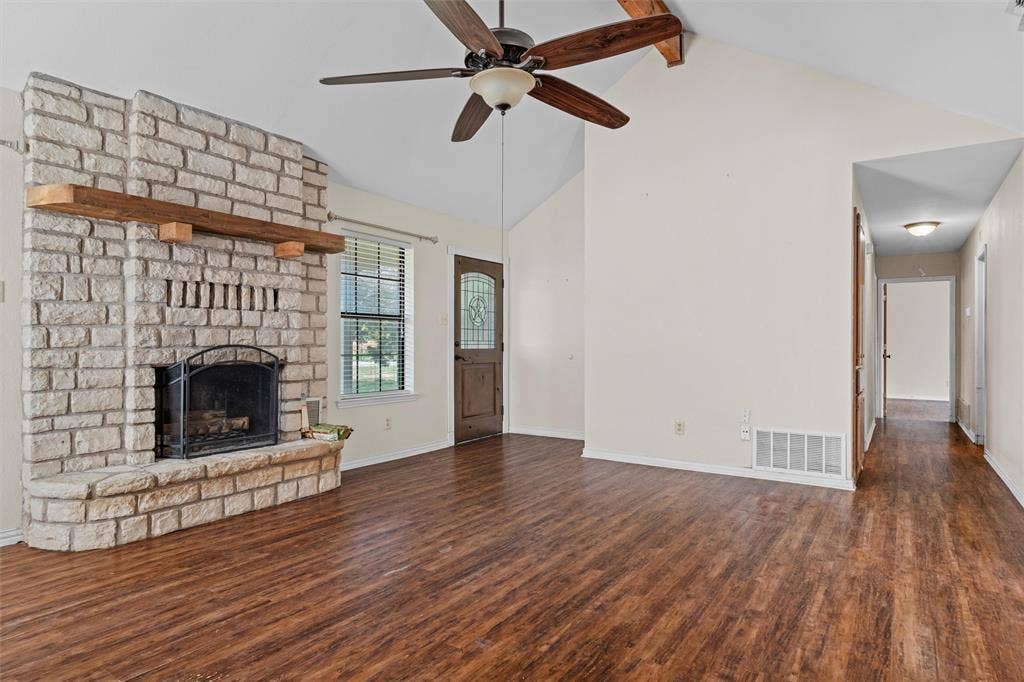 Vaulted ceilings featuring a prominent wooden beam, stone fireplace with a thick timber mantel, and wood-finish flooring