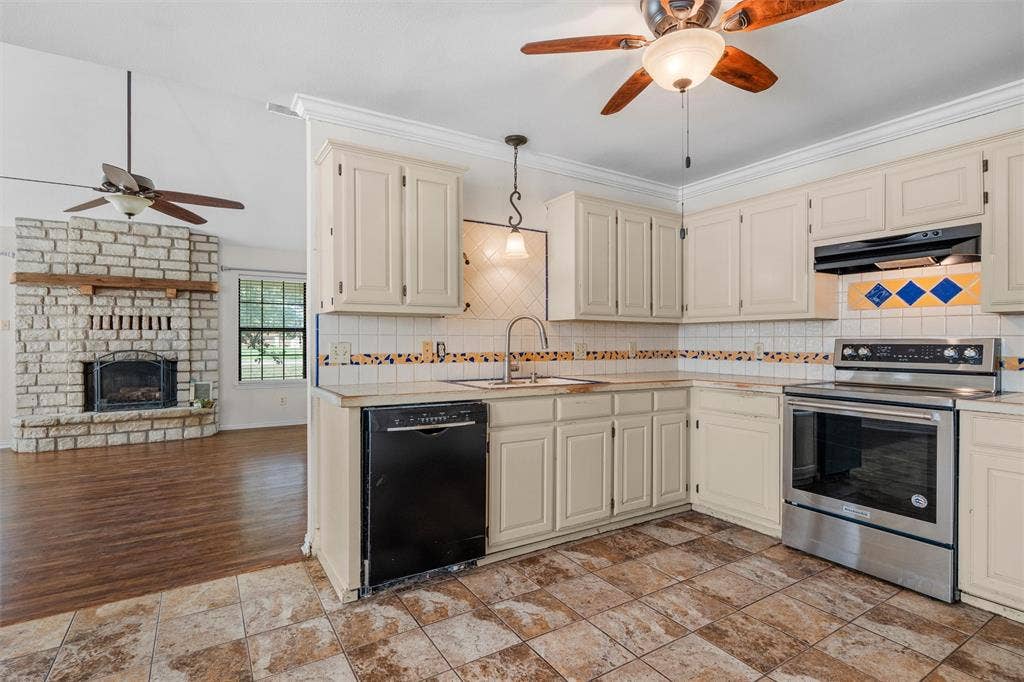 Kitchen featuring light cabinetry, stainless steel appliances, and tiled flooring, accented by a stone fireplace with a wood mantel