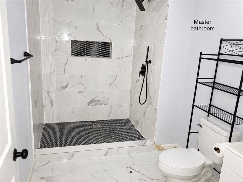 709 SW Dallas Street, Grand Prairie, TX 75051 Walk-in shower featuring large-format stone-patterned wall tile, a mosaic-tiled floor, a built-in recessed wall niche, and matte black plumbing fixtures