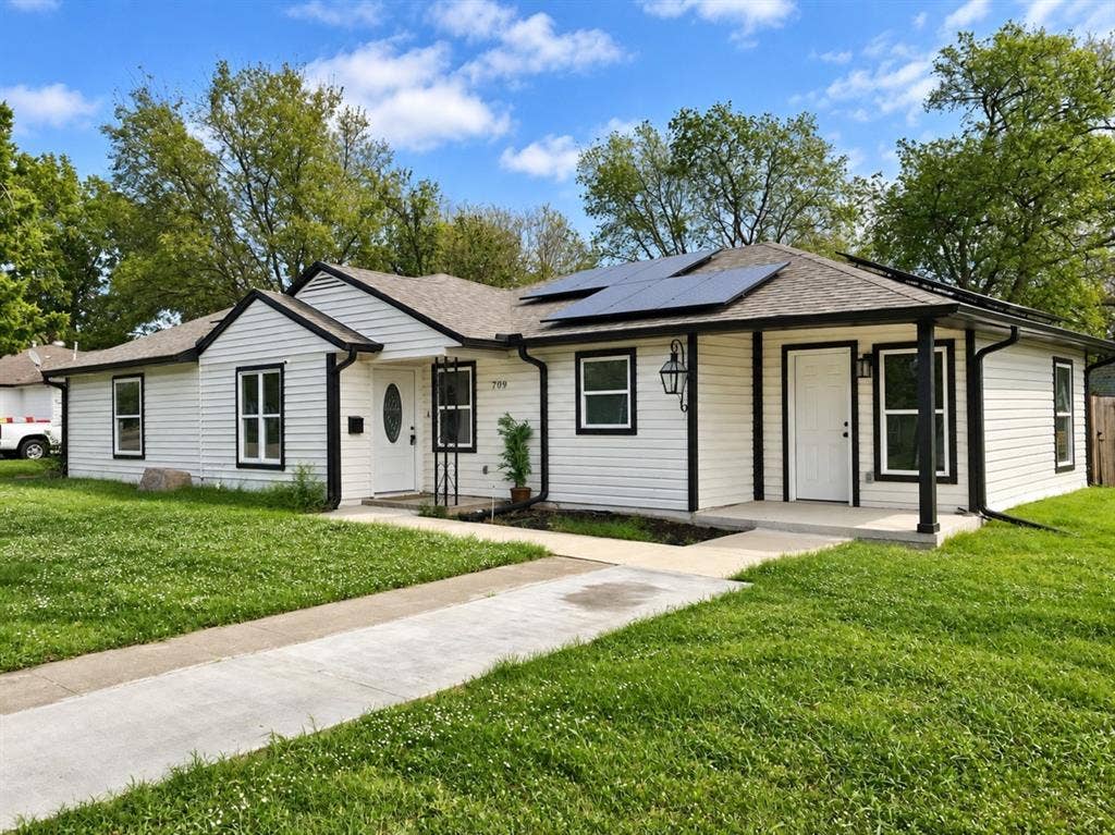 709 SW Dallas Street, Grand Prairie, TX 75051 Exterior featuring white horizontal siding, black window trim, roof-mounted solar panels, and a covered concrete entry porch