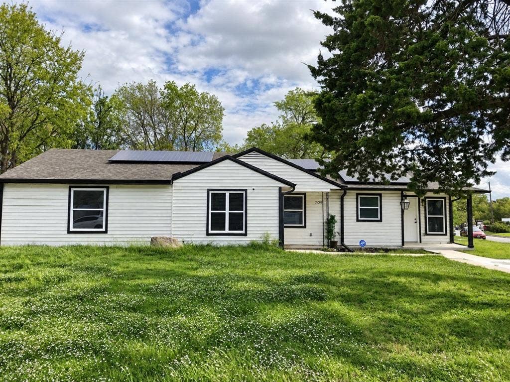709 SW Dallas Street, Grand Prairie, TX 75051 Single-story exterior featuring white horizontal siding, contrasting dark trim, a roof-mounted solar panel system, and a concrete walkway