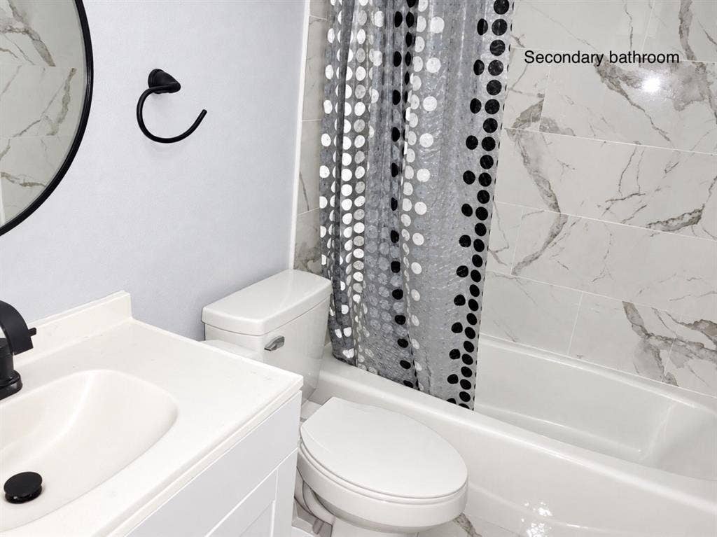 709 SW Dallas Street, Grand Prairie, TX 75051 Bathroom featuring a white vanity with integrated sink, matte black faucet, wall-mounted circular mirror, and tile surround bathtub