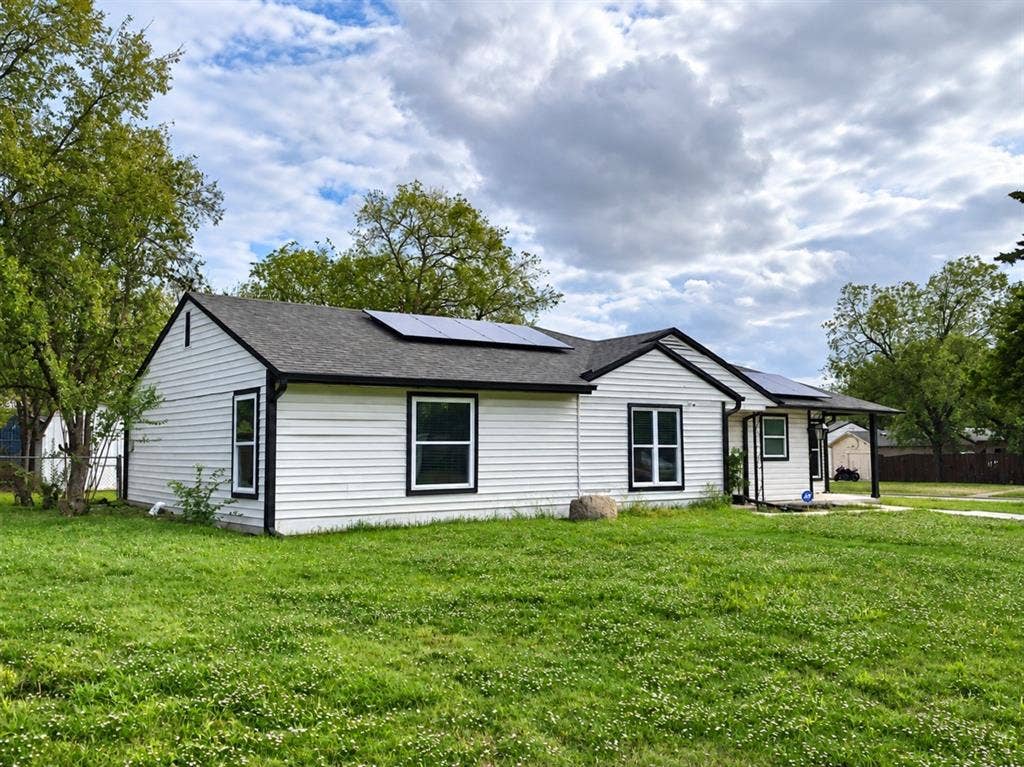 709 SW Dallas Street, Grand Prairie, TX 75051 Single-story residence featuring white horizontal siding, a dark shingle roof, roof-mounted solar panels, and a covered front porch entrance