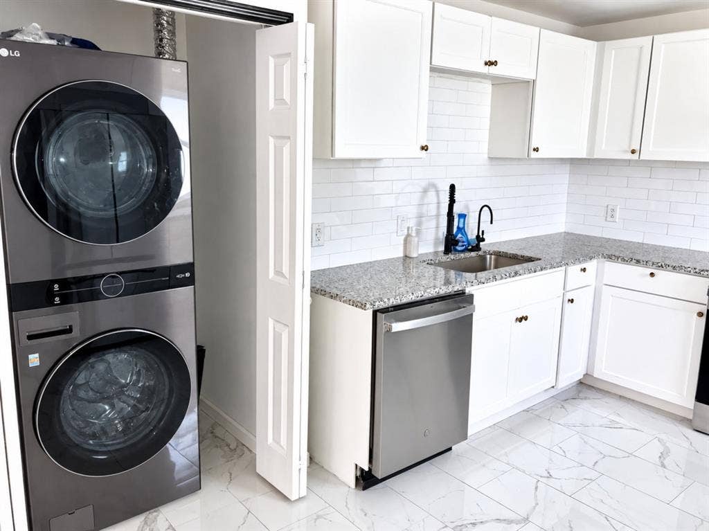 709 SW Dallas Street, Grand Prairie, TX 75051 Kitchen featuring shaker-style white cabinetry, stone-finish countertops, subway tile backsplash, stainless steel dishwasher, and large-format tile flooring with marble-finish veining