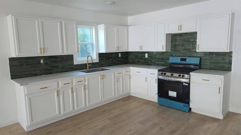 3426 Edgewood Street, Dallas, TX 75215 Kitchen featuring white cabinetry with gold-tone hardware, green tile backsplash, light-toned solid surface countertops, and wood-finish flooring