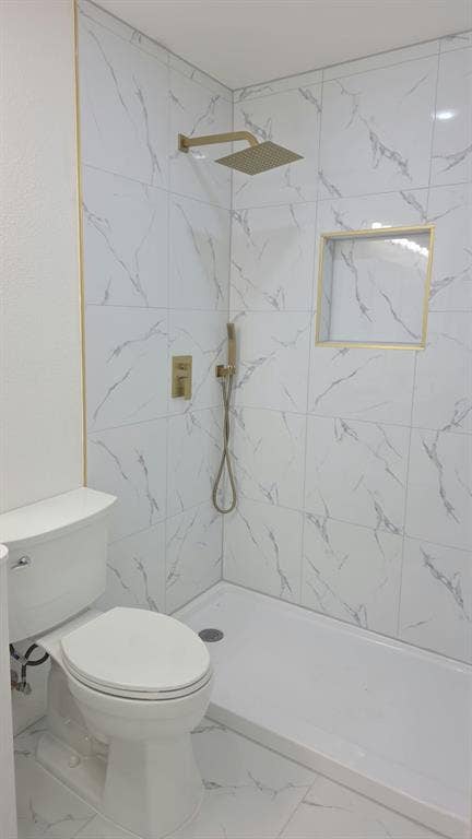 3426 Edgewood Street, Dallas, TX 75215 Shower stall featuring white stone-finish tile surround with gold-toned trim, built-in recessed wall niche, rainfall showerhead, and a secondary handheld sprayer with a matching gold-toned finish