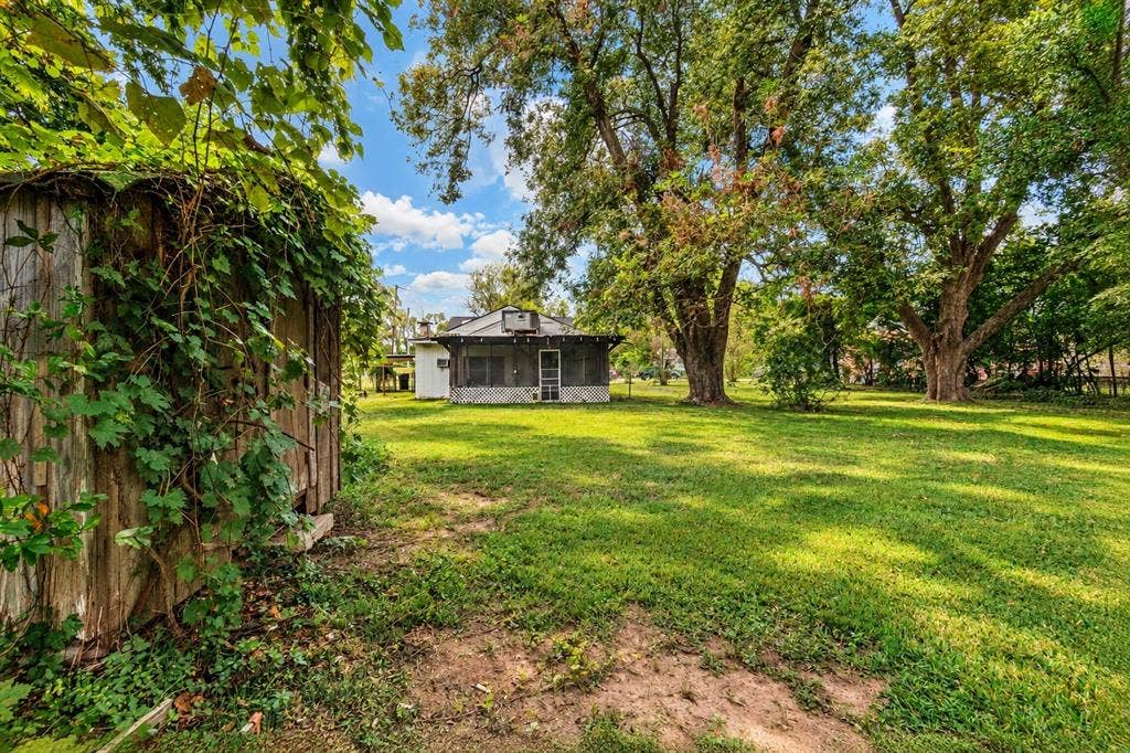 Expansive lot featuring mature trees, a detached wood-frame storage structure, and a screen-enclosed porch