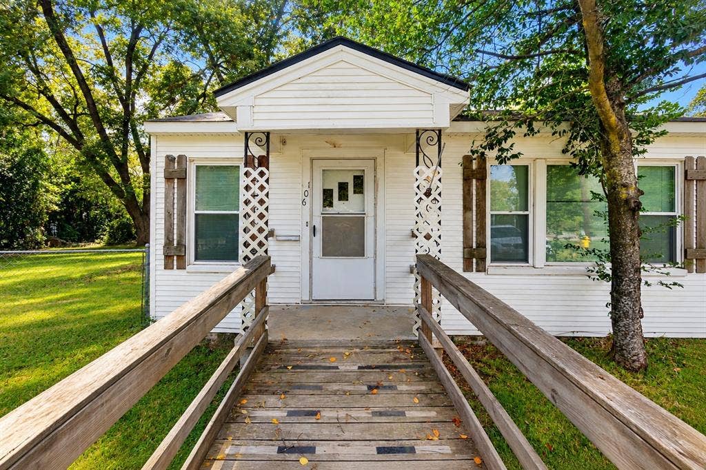White siding exterior featuring decorative shutters, a covered front entryway, lattice porch accents, and a wooden ramp