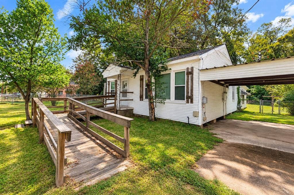 White lap siding exterior featuring decorative wooden shutters, an attached metal-roof carport, and a wooden entry ramp