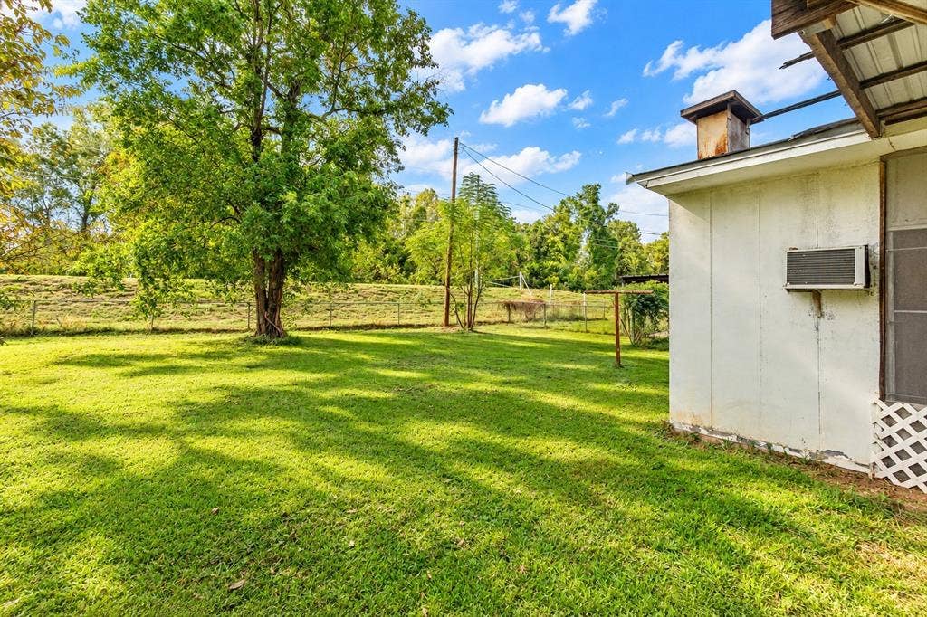 Expansive backyard featuring a large mature tree, open grass space, and metal-frame perimeter fencing