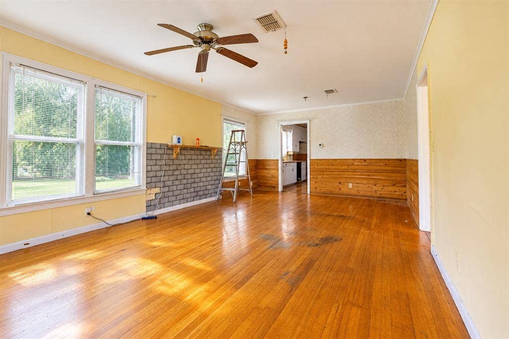 Living area featuring wood-finish flooring, wood wall paneling, a ceiling fan, and a masonry-style fireplace surround