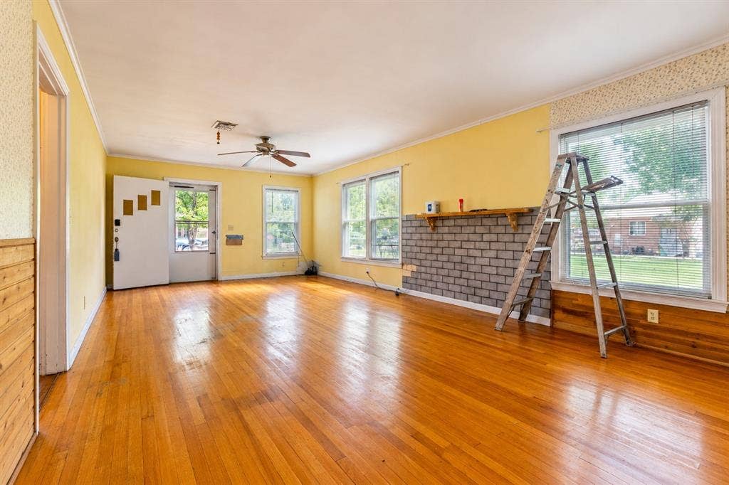 Open-concept living space featuring wood-finish flooring, a textured brick fireplace with a wood mantel, multi-pane windows, and a ceiling fan