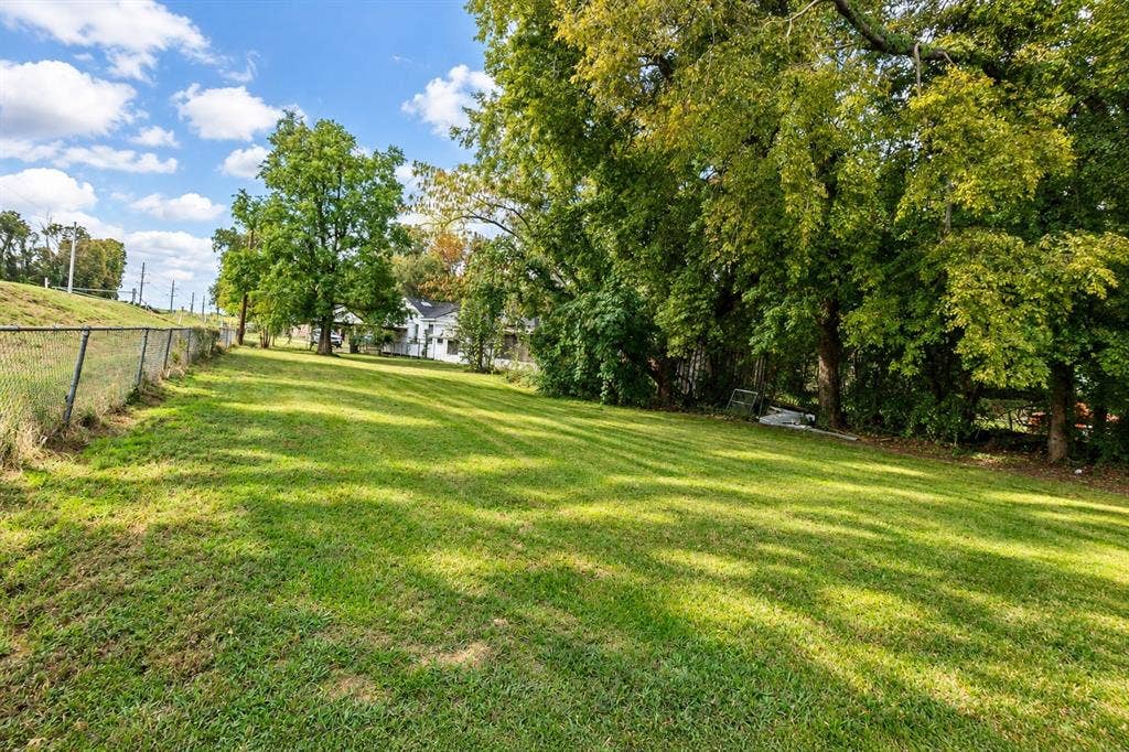 Expansive grassy lawn featuring mature trees, perimeter chain-link fencing, and a sloping terrain