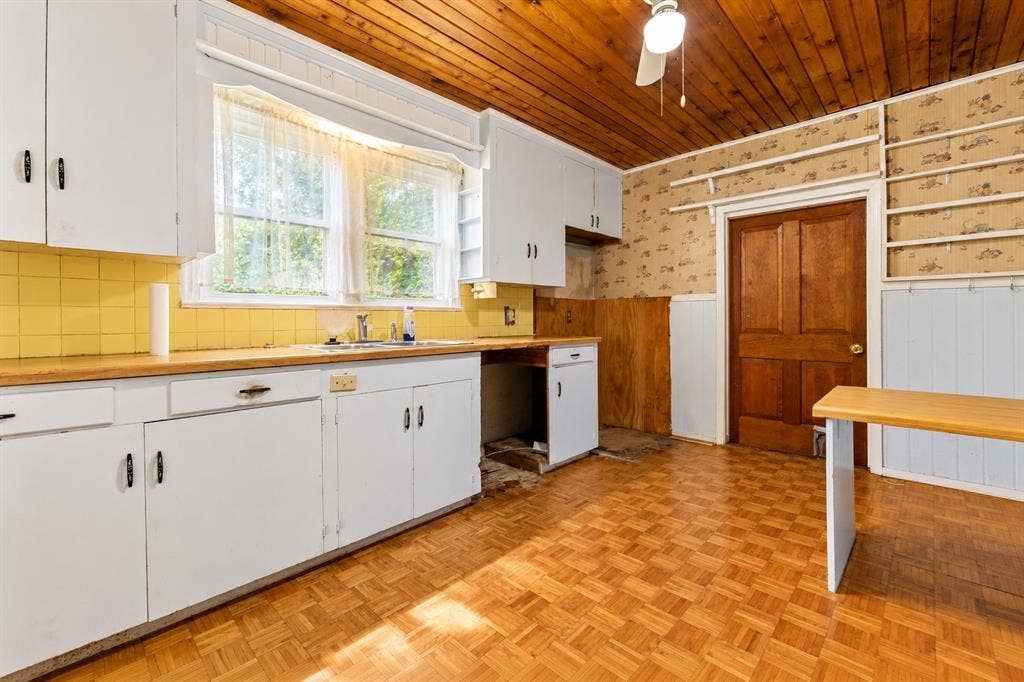 Kitchen featuring wood-panel ceiling, parquet flooring, white cabinetry, tile backsplash, and solid wood door