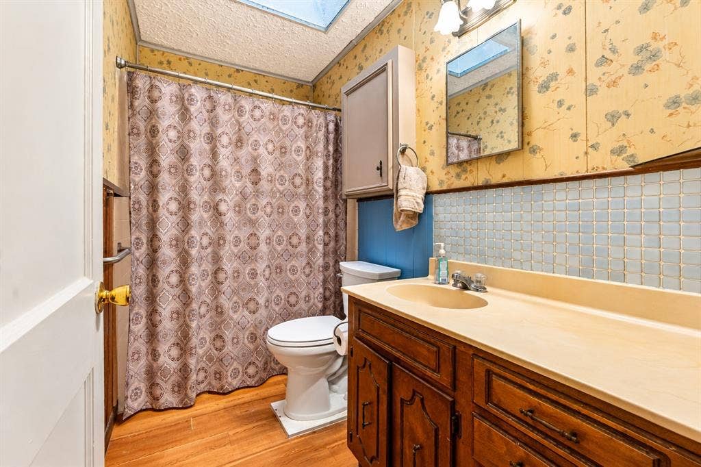 Bathroom featuring a skylight, wood-finish flooring, a vanity with an integrated countertop sink, a tile backsplash, and a built-in medicine cabinet