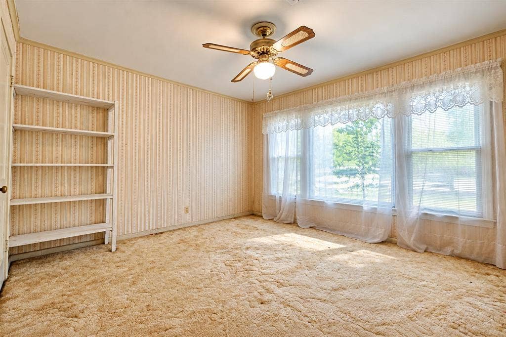 Room featuring a large bay window, wall-to-wall carpeting, built-in shelving, and a ceiling fan with light fixture