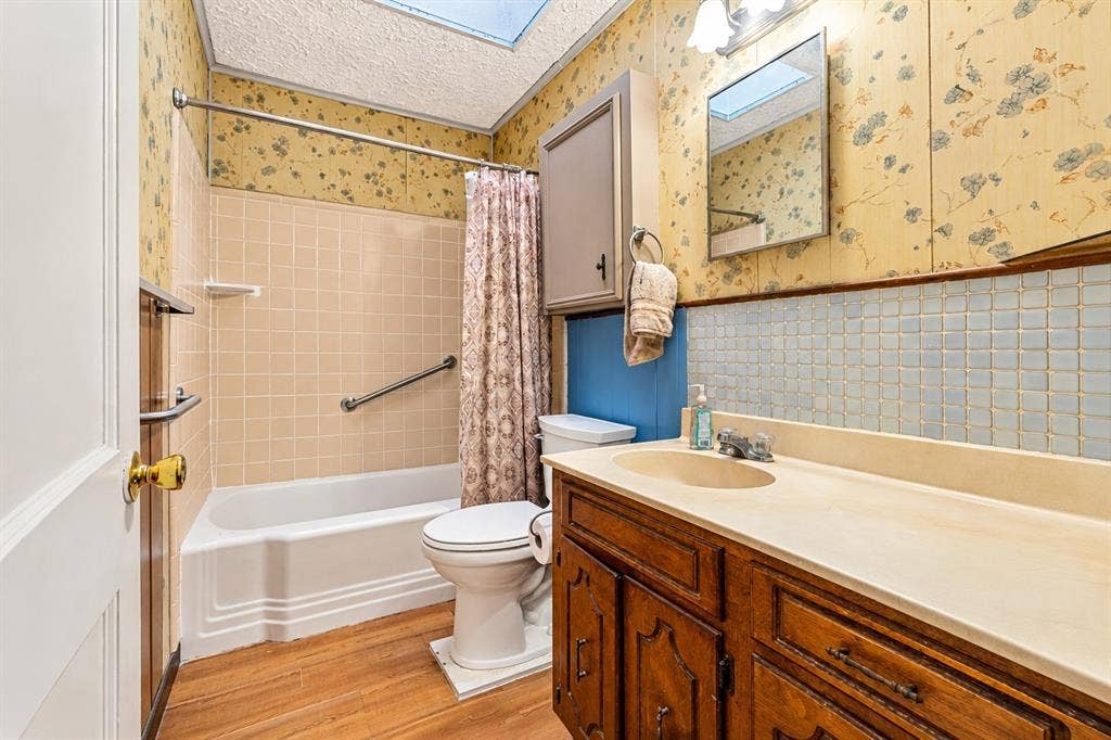Bathroom featuring a skylight, tile-surround bathtub, built-in medicine cabinet, wood-finish vanity with an integrated countertop, and square mosaic wall tiling