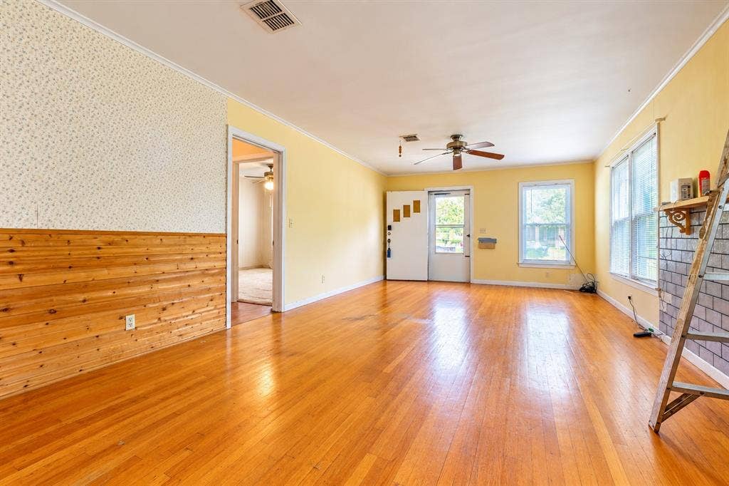 Wood-finish flooring, horizontal wood-paneled wall accent, ceiling fan, and brick-surround fireplace
