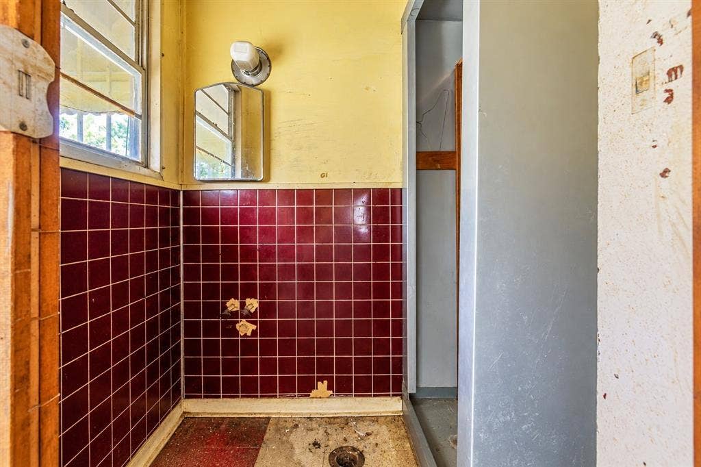 Half-wall of glossy burgundy ceramic tiling, multi-pane window, wall-mounted light fixture, and walk-in shower stall