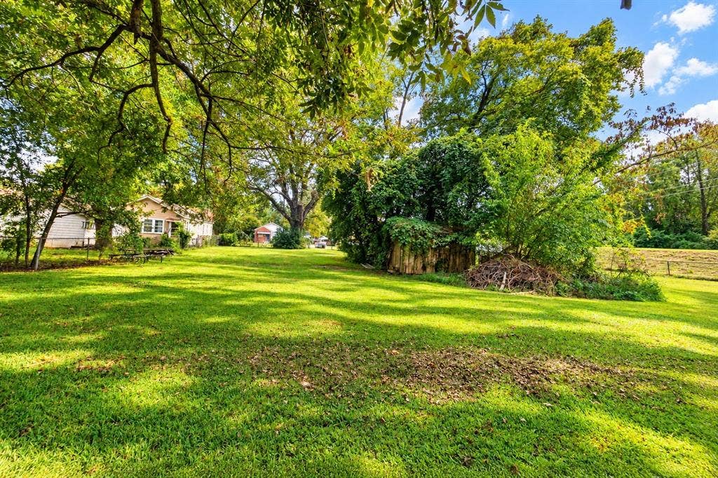 Expansive lawn area featuring mature trees and a wood-structure storage building